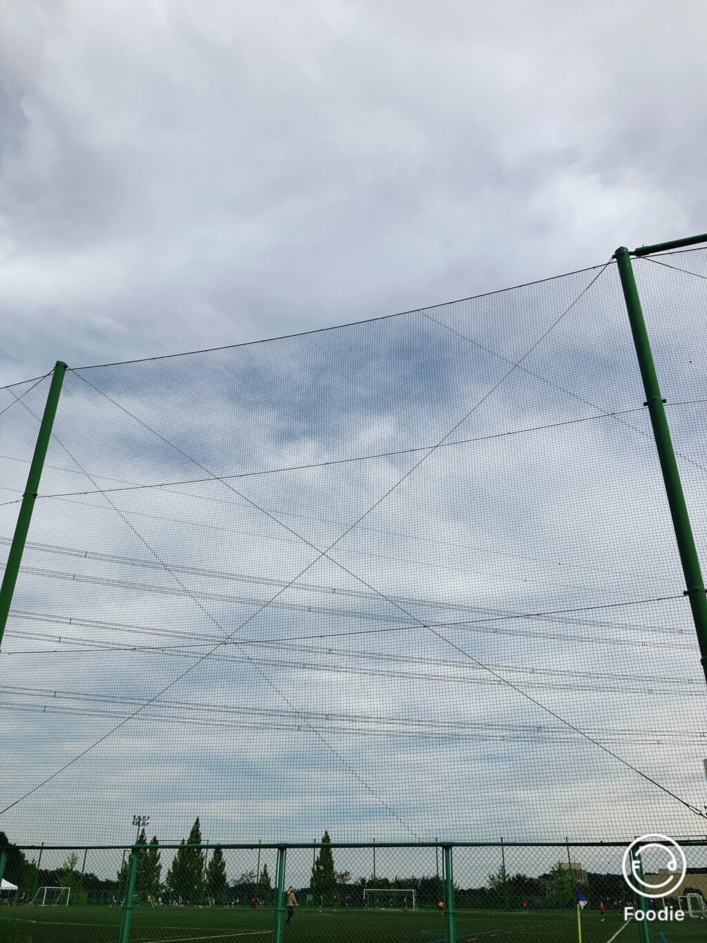 サッカーグラウンドの上に広がる曇り空。秋らしい優しい光の中、ネット越しに見えるフィールドの風景。