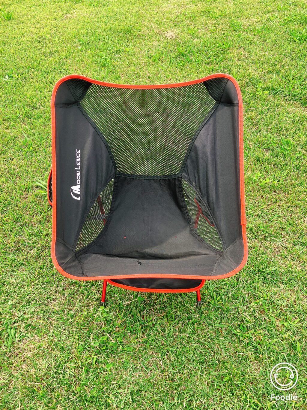 芝生の上に置かれた黒とオレンジの折りたたみチェア。通気性のあるメッシュ素材で軽量タイプ。