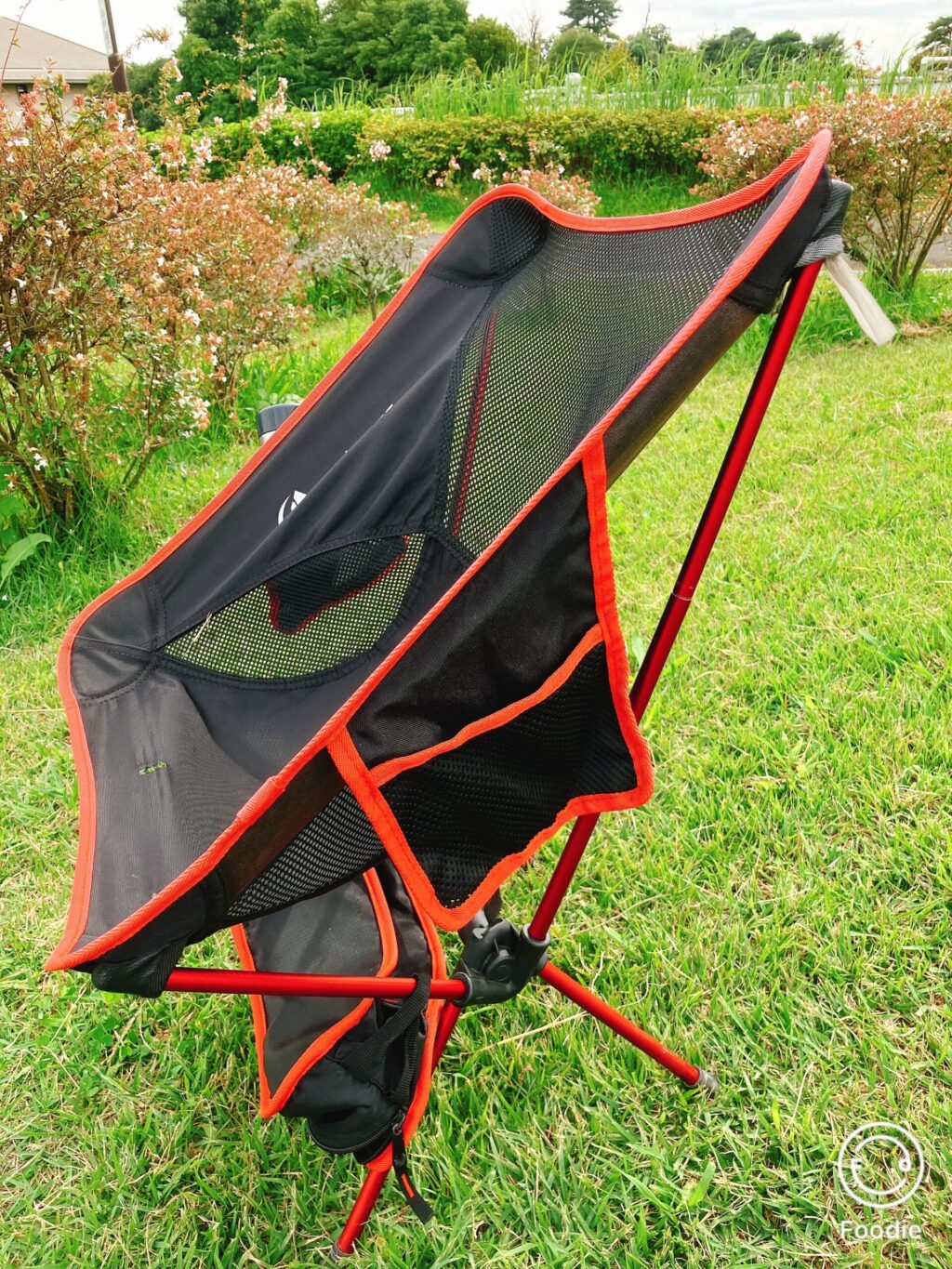 側面から見た折りたたみアウトドアチェア。赤いフレームとメッシュ素材の組み合わせが印象的。