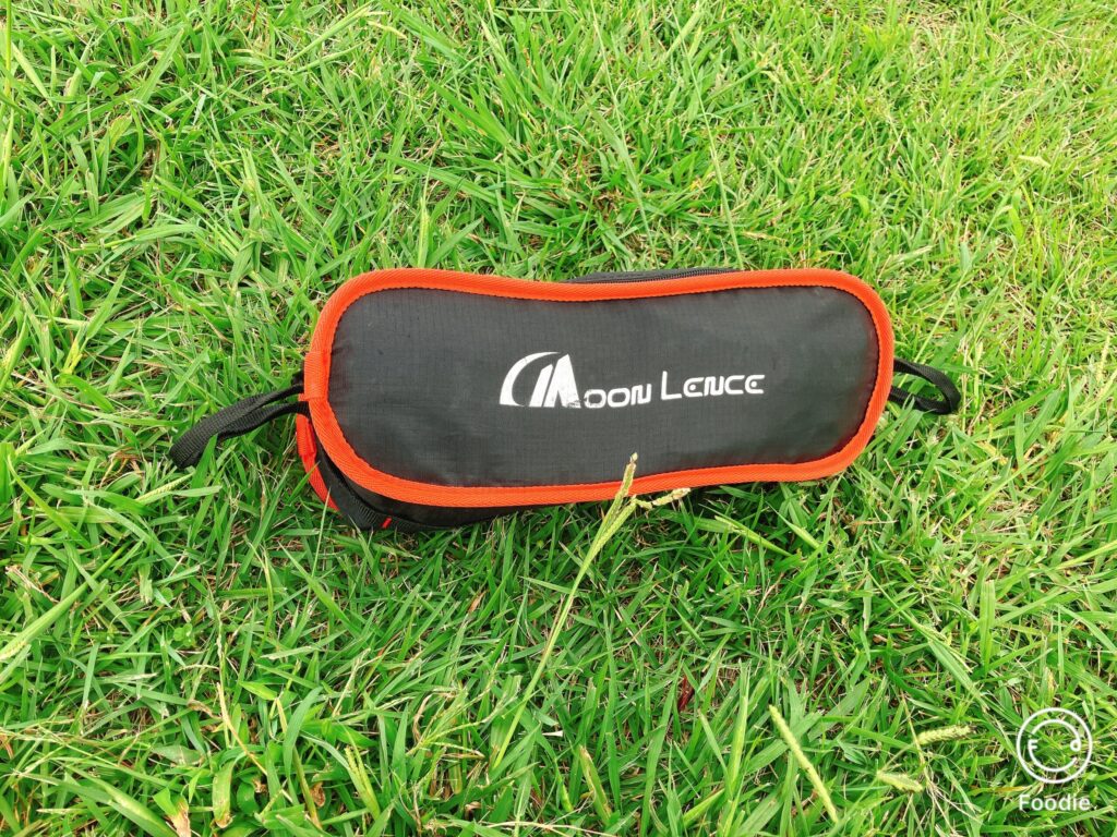 芝生の上に置かれた折りたたみチェアの収納ケース。黒地にオレンジの縁取りがアクセントになっている。