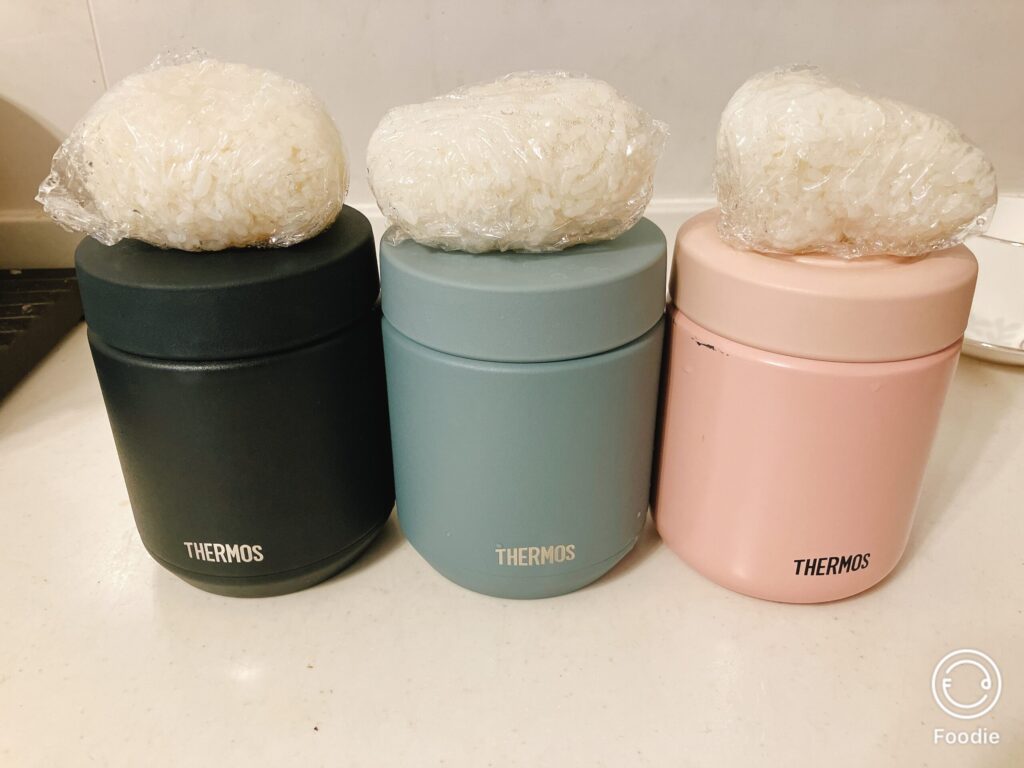 サーモスのスープジャー3色（黒・ブルー・ピンク）と白おにぎりを並べた写真